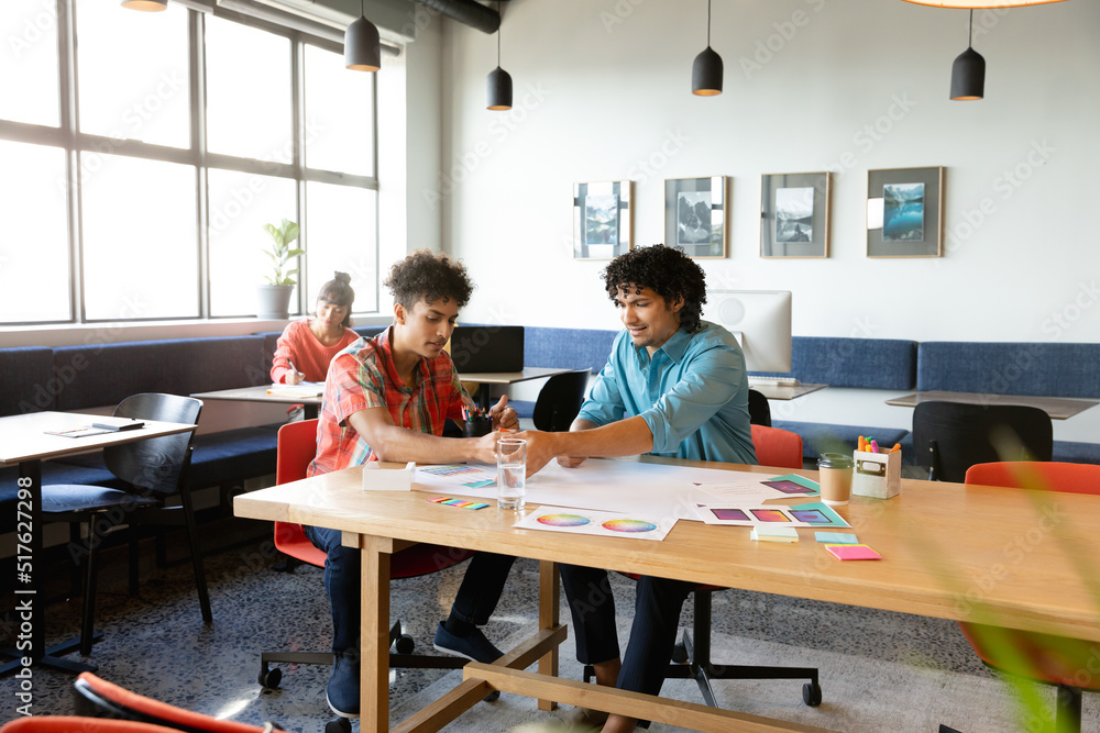 Creative biracial colleagues discussing over charts at table in office Creative biracial colleagues discussing over charts at table in office