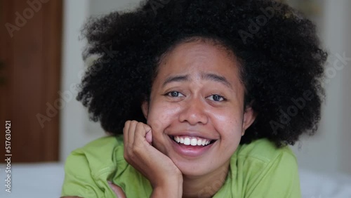 A happy black woman close-up with an afro hairstyle lies on the bed and smiles with a snow-white smile and sings songs. Portrait of afroasian woman in bedroom on bed home interior. photo