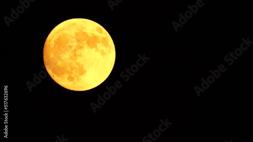 Glowing yellow huge full moon as seen from earth through the clouds against starry night sky. Large full moon moves across the sky, moon makes its way from bottom left frame to top right. photo