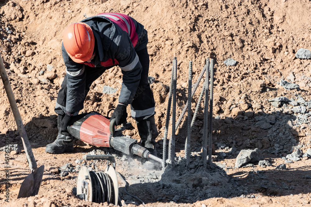 A worker with a jackhammer breaks concrete piles. Felling the pile head with a hand tool. Preparation of piles for mounting the foundation. A worker with a jackhammer breaks concrete piles. Felling the pile head with a hand tool. Preparation of piles for mounting the foundation.