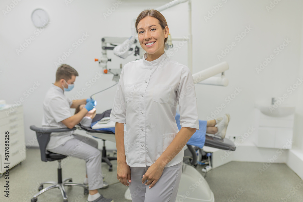 A woman dentist smiles at the camera on the background of a dental cabinet. Dental care and treatment concept A woman dentist smiles at the camera on the background of a dental cabinet. Dental care and treatment concept