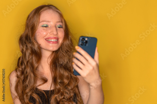 Young red haired girl with braces smiling joyfully and happy looking at new phone with cash back message. Black friday and cyber monday discount concept
