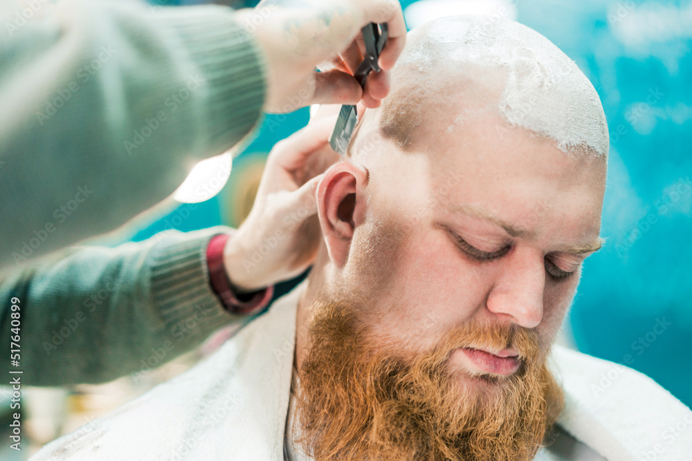 Fototapeta premium A sleeping bearded client during shaving in barbershop.