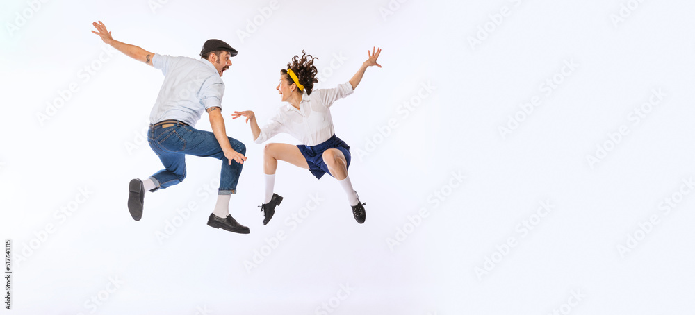 Portrait of young active couple, man and woman, dancing, jumping isolated over white studio background. Flyer