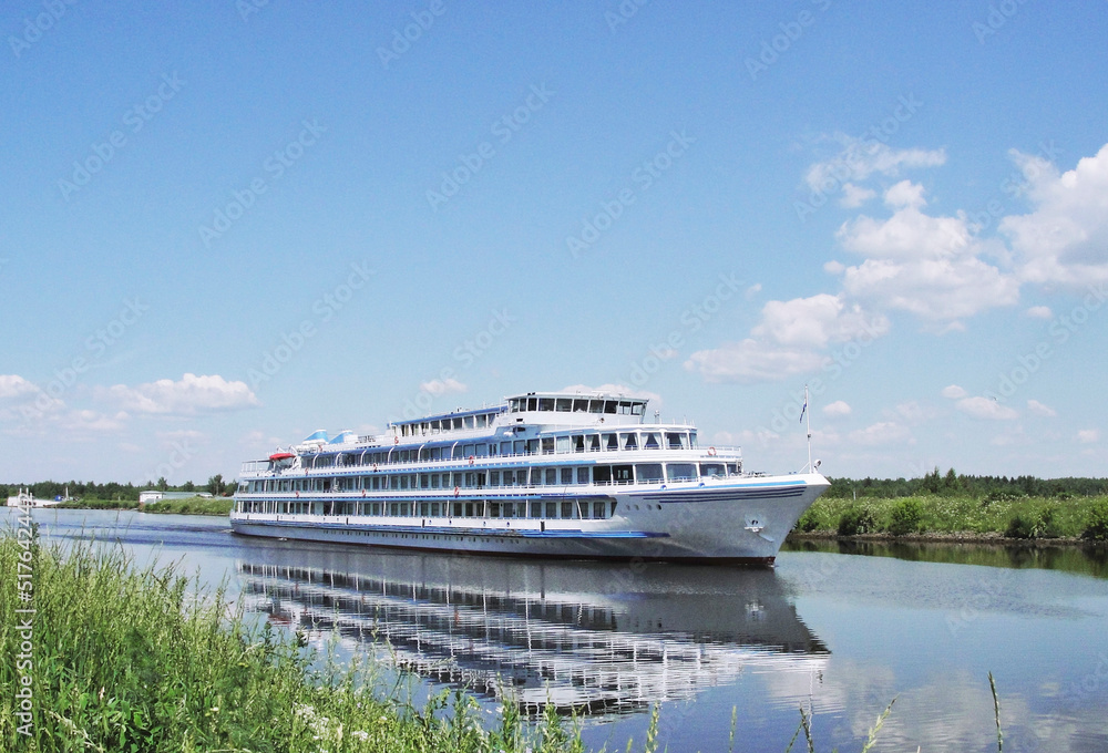 A white ship sails along the river on a clear summer day. 