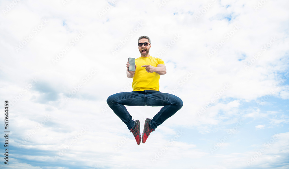 amazed man jumping and presenting smartphone on sky background amazed man jumping and presenting smartphone on sky background