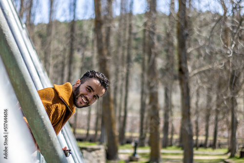 A young man smiling while leaning out from a pedestrian bridge in nature