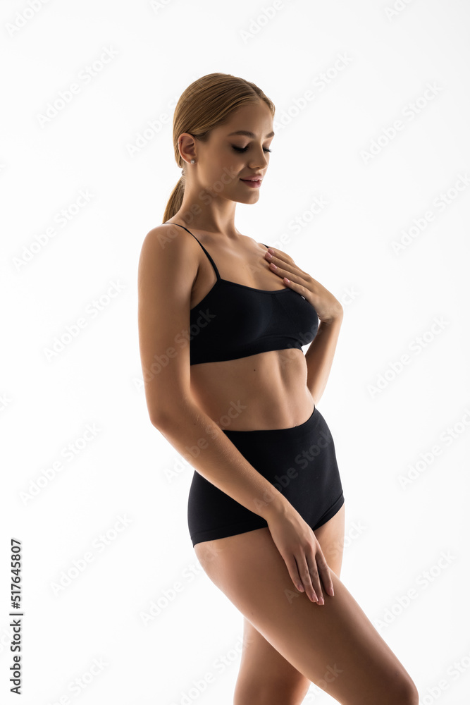 Laughing sporty girl in black bikini posing on grey background. Attractive girl with slim toned body. Beauty and body care concept Laughing sporty girl in black bikini posing on grey background. Attractive girl with slim toned body. Beauty and body care concept