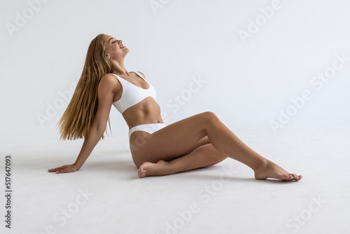 Sitting on the floor. Beautiful woman with slim body in underwear on white background