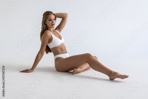 Young beautiful woman with perfect body in underwear sitting on floor posing on white studio background. Body care, female beauty, spa concept © F8  \ Suport Ukraine