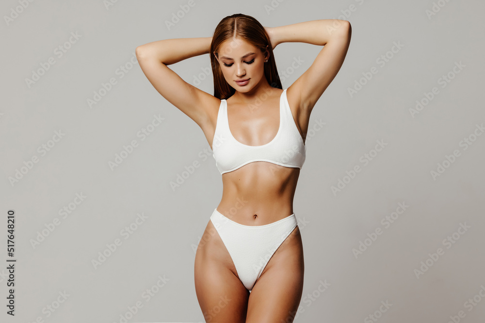 Proud of her perfect body. Attractive young woman in white lingerie posing against grey background and smiling - obrazy, fototapety, plakaty 