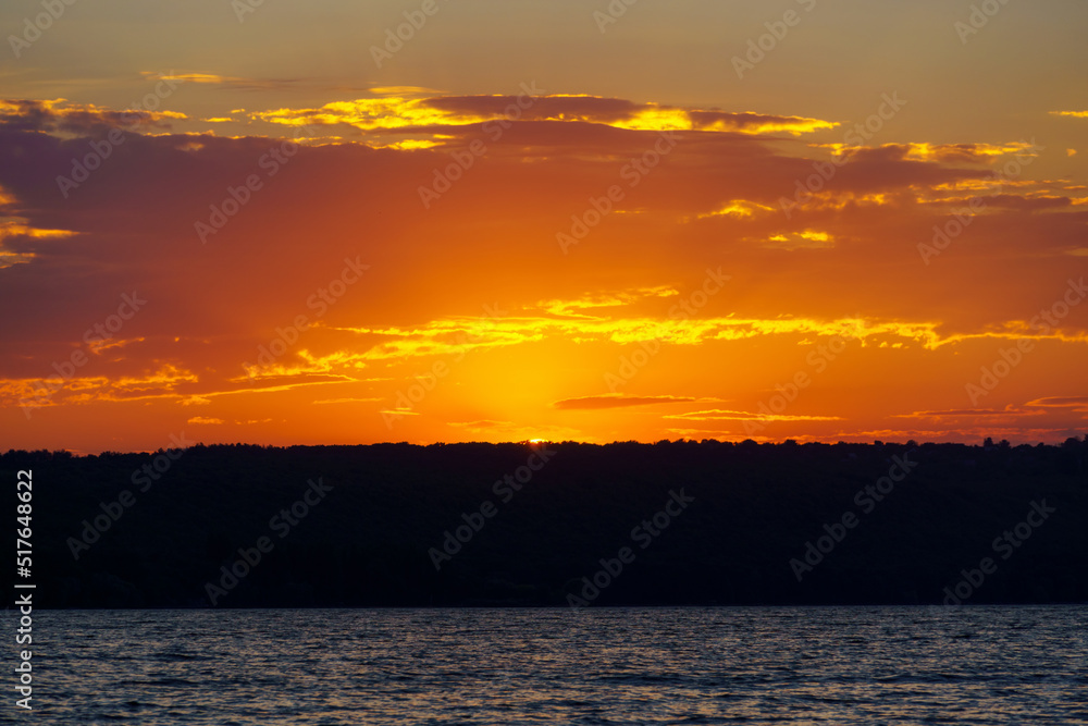 sunset over the lake, bright sun reflected in the waves, glare on the water, beautiful summer landscape