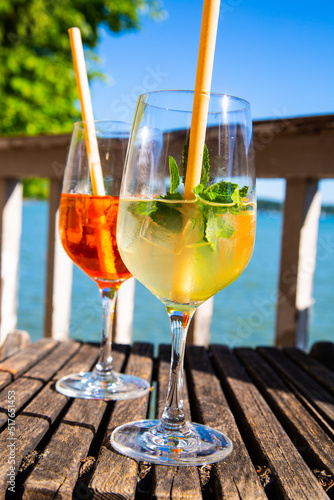 Hugo and Aperol Sprizz together on a wooden table, with the Ammersee in the background