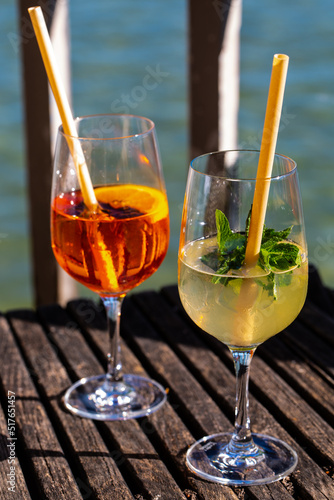 Hugo and Aperol Sprizz together on a wooden table, with the Ammersee in the background