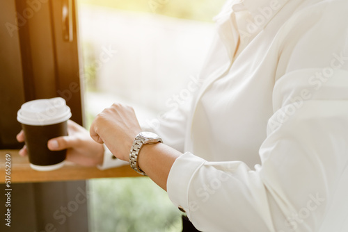 Close up hands checking time on her watch and holding hot coffee cup. Business looking on her wristwatch for waiting someone.