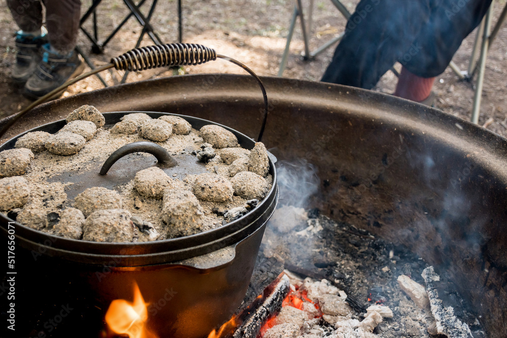 Dutch oven camp cooking with coal briquettes beads on top. Campfire in