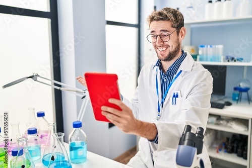 Hispanic man with beard working at scientist laboratory doing video call celebrating achievement with happy smile and winner expression with raised hand