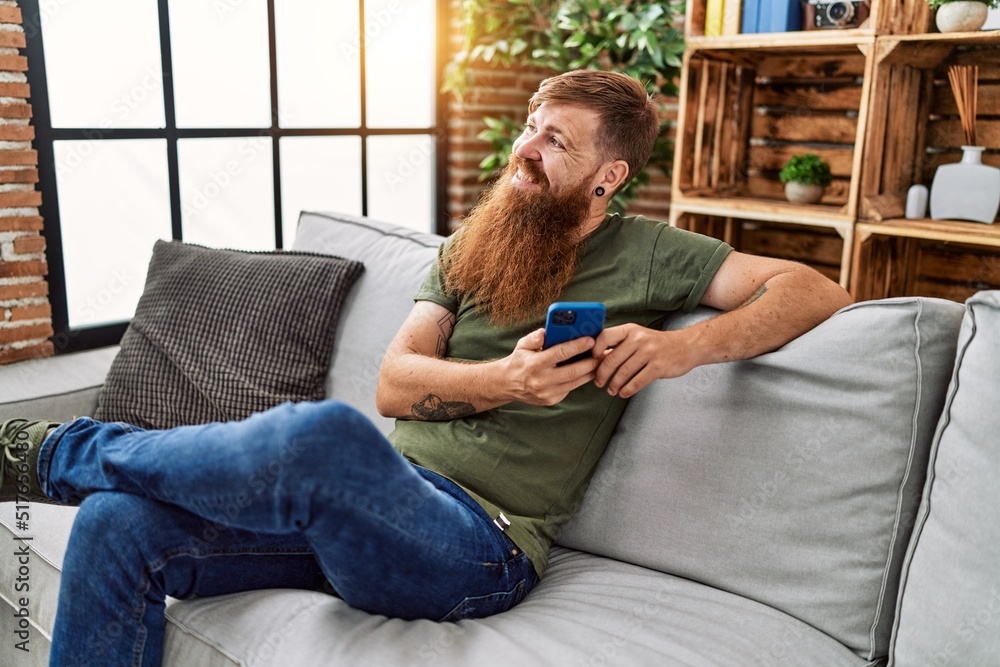 Obraz premium Young redhead man smiling confident using smartphone at home