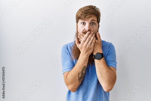 Caucasian man with long beard standing over isolated background shocked covering mouth with hands for mistake. secret concept.