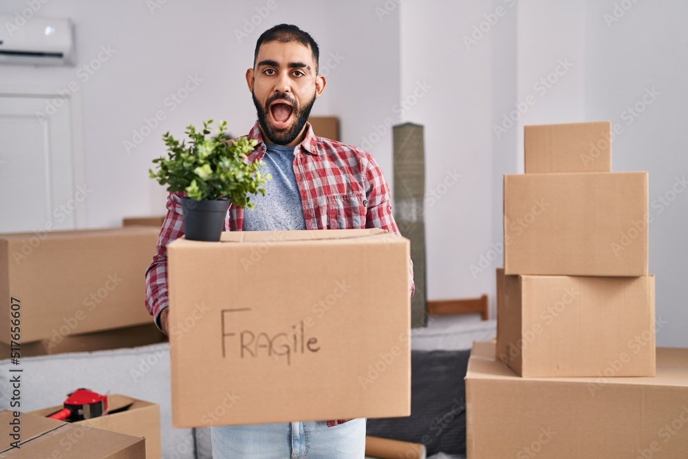 Middle east man with beard moving to a new home holding cardboard box celebrating crazy and amazed for success with open eyes screaming excited. Middle east man with beard moving to a new home holding cardboard box celebrating crazy and amazed for success with open eyes screaming excited.