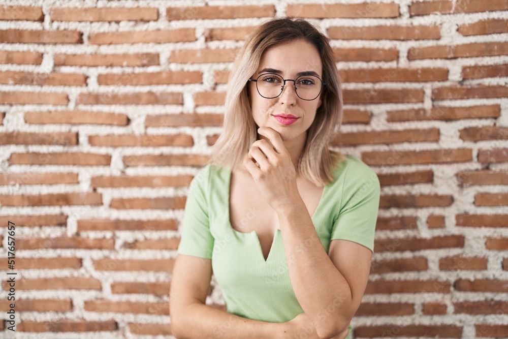 Young beautiful woman standing over bricks wall looking confident at the camera with smile with crossed arms and hand raised on chin. thinking positive. Young beautiful woman standing over bricks wall looking confident at the camera with smile with crossed arms and hand raised on chin. thinking positive.