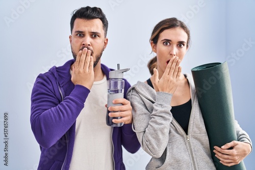 Young hispanic couple wearing sportswear covering mouth with hand, shocked and afraid for mistake. surprised expression