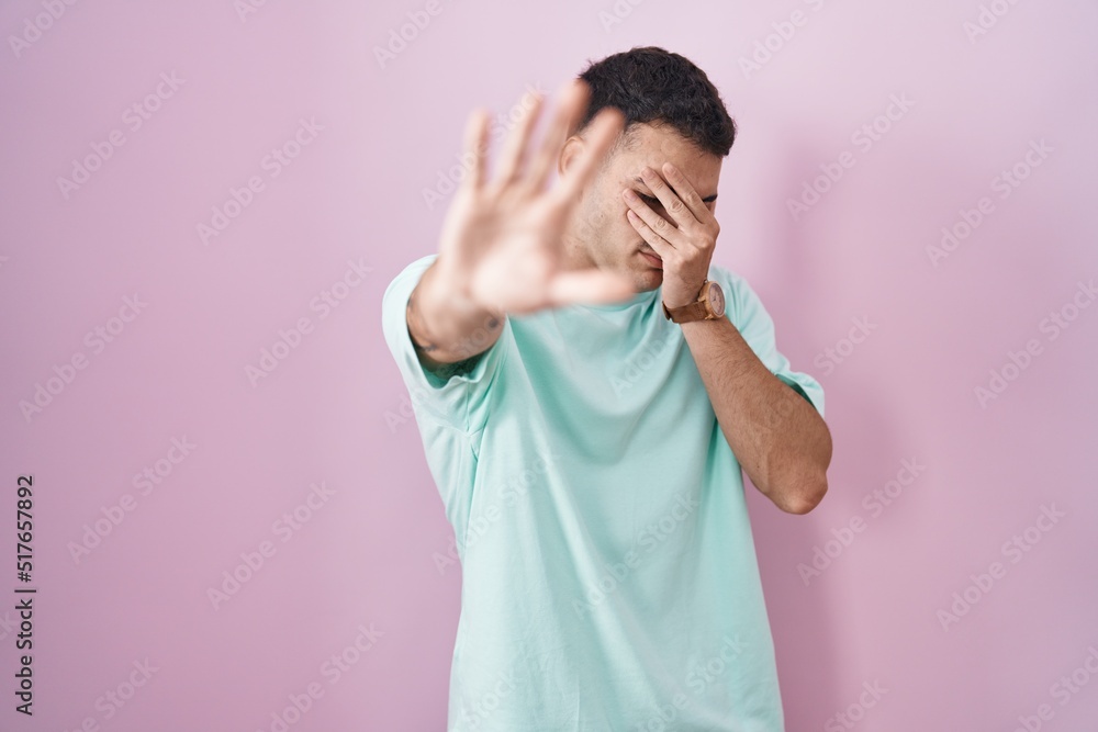 Handsome hispanic man standing over pink background covering eyes with hands and doing stop gesture with sad and fear expression. embarrassed and negative concept. Handsome hispanic man standing over pink background covering eyes with hands and doing stop gesture with sad and fear expression. embarrassed and negative concept.