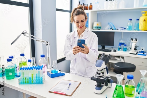 Young woman wearing scientist uniform using smartphone at laboratory