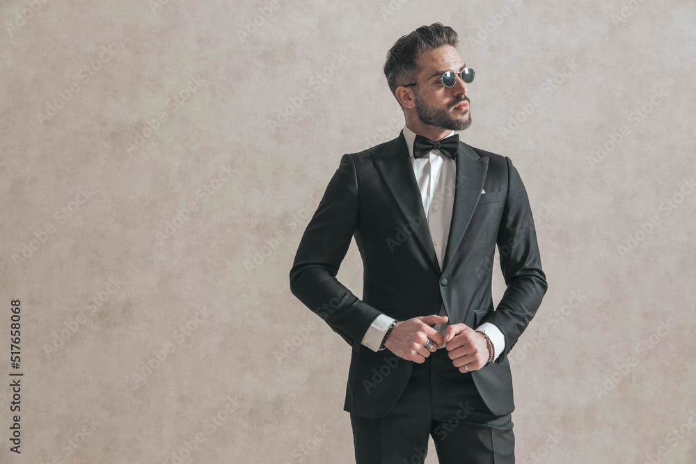 attractive elegant man looking to side while adjusting black tuxedo attractive elegant man looking to side while adjusting black tuxedo