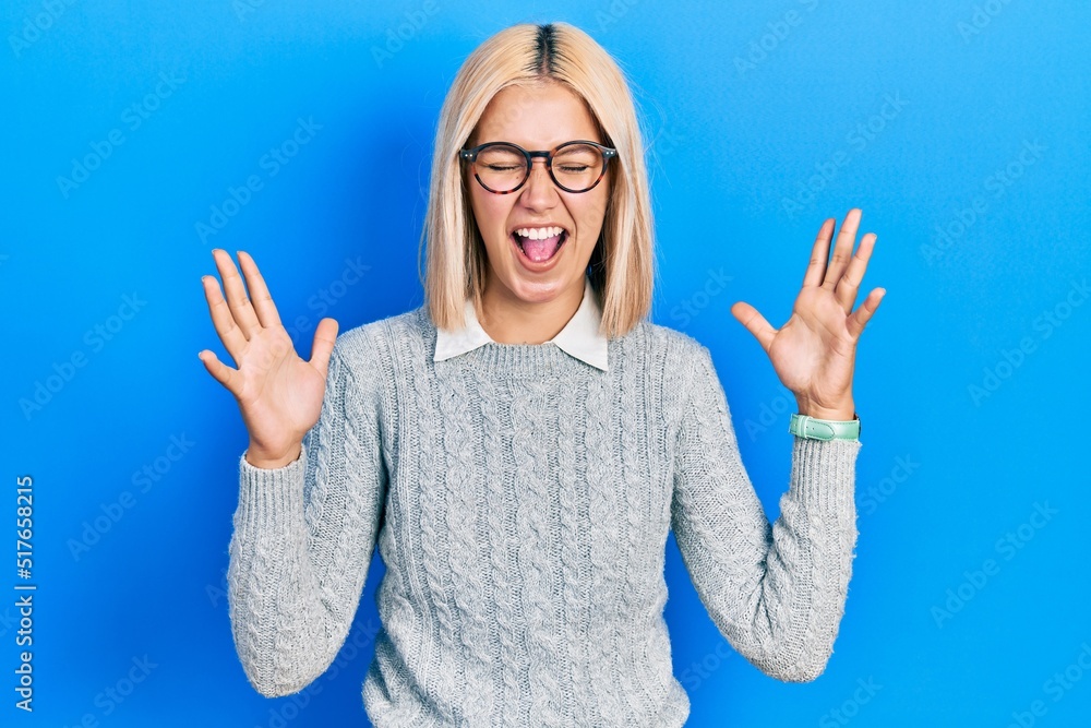 Beautiful blonde woman wearing glasses celebrating mad and crazy for success with arms raised and closed eyes screaming excited. winner concept Beautiful blonde woman wearing glasses celebrating mad and crazy for success with arms raised and closed eyes screaming excited. winner concept