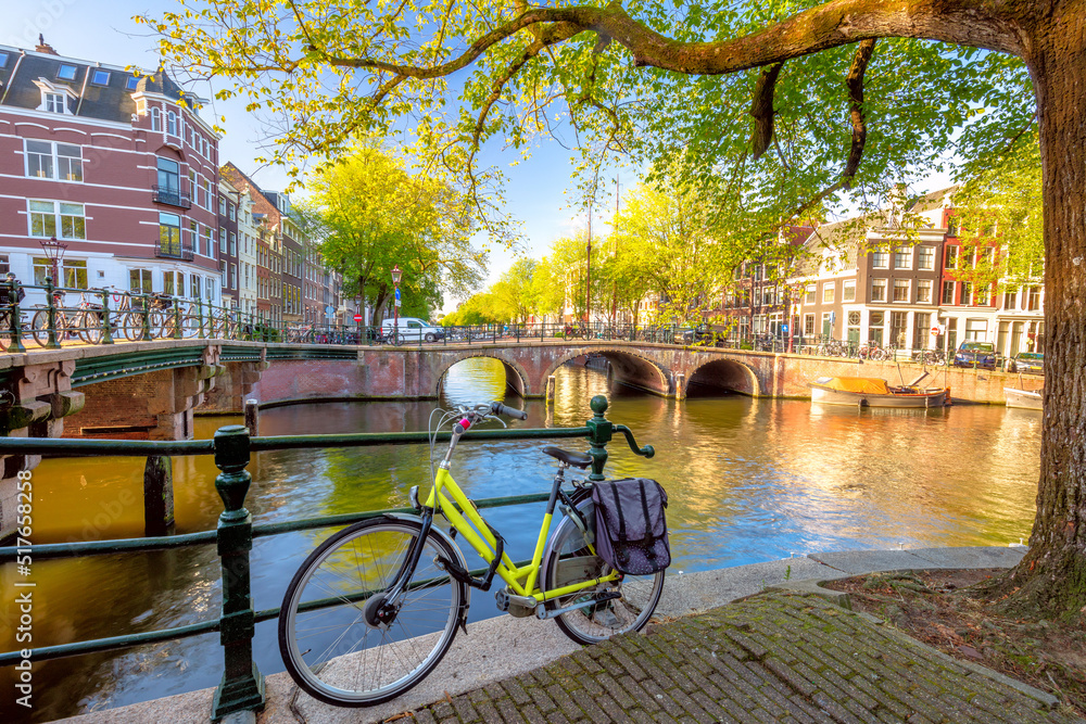 Early quiet morning in Amsterdam. Ancient houses, a bridge, traditional bicycles, canals and the sun shines through the trees. Lovely morning in Amsterdam.