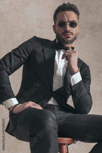 cool businessman in black tuxedo holding elbow on knee and sitting