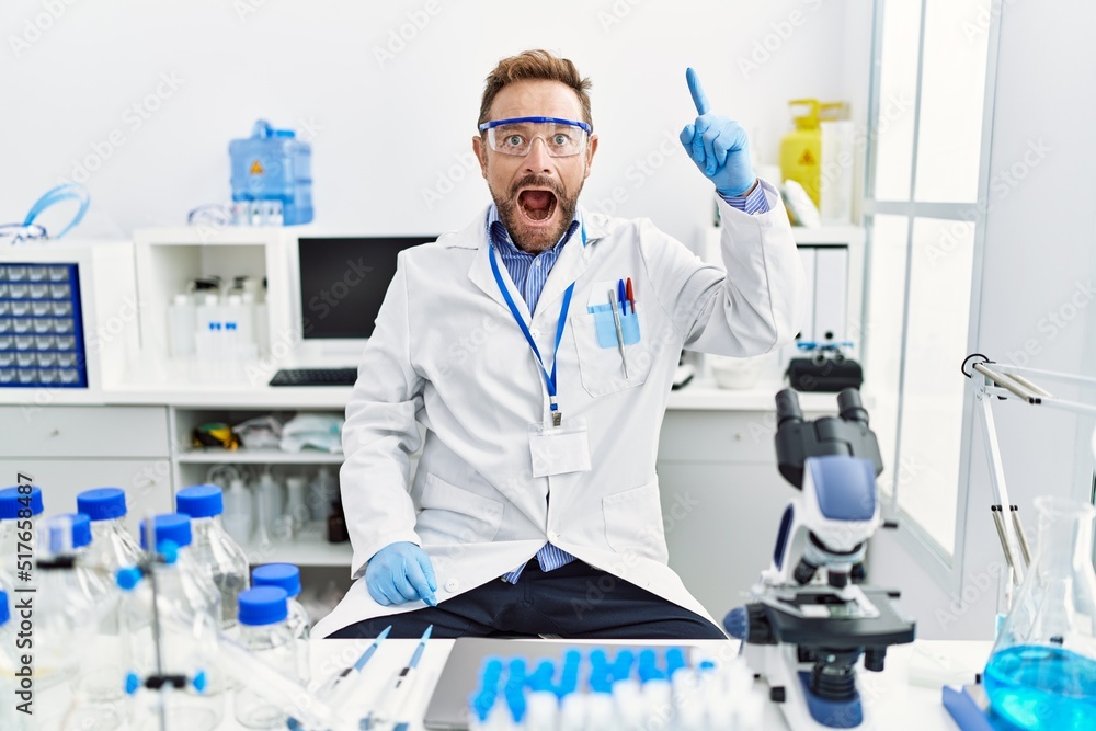 Middle age man working at scientist laboratory pointing finger up with successful idea. exited and happy. number one. Middle age man working at scientist laboratory pointing finger up with successful idea. exited and happy. number one.
