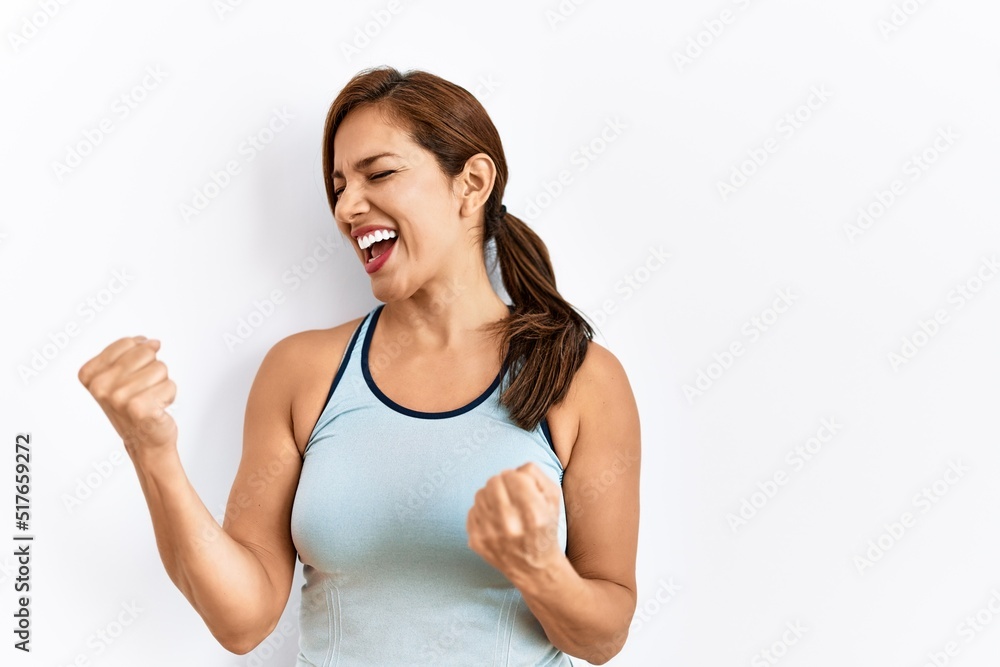 Young latin woman wearing sporty clothes over isolated background very happy and excited doing winner gesture with arms raised, smiling and screaming for success. celebration concept. Young latin woman wearing sporty clothes over isolated background very happy and excited doing winner gesture with arms raised, smiling and screaming for success. celebration concept.