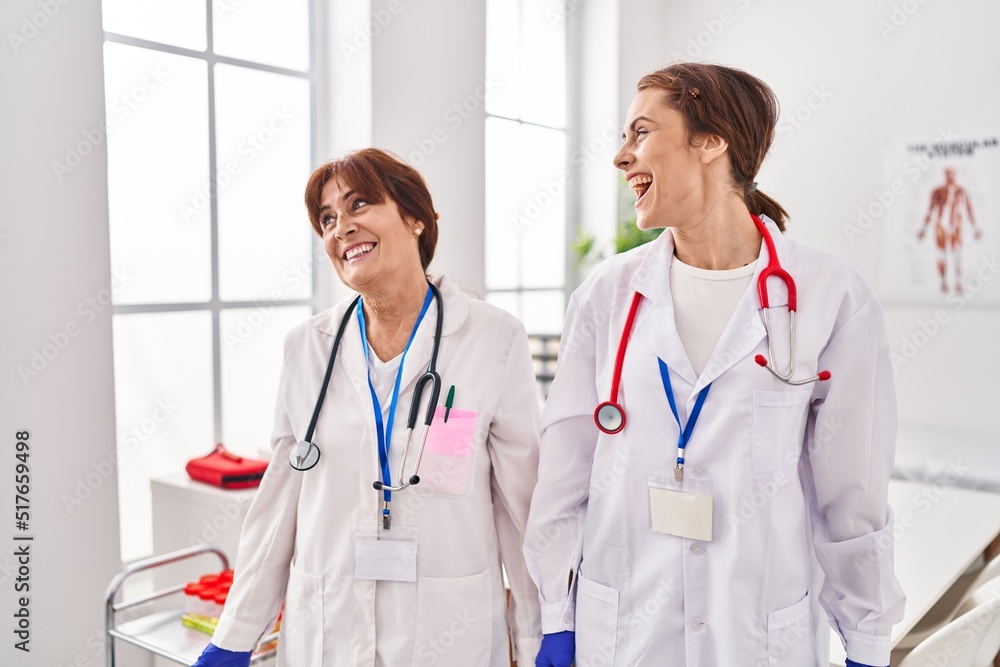 Two women wearing doctor uniform and stethoscope looking away to side with smile on face, natural expression. laughing confident. Two women wearing doctor uniform and stethoscope looking away to side with smile on face, natural expression. laughing confident.