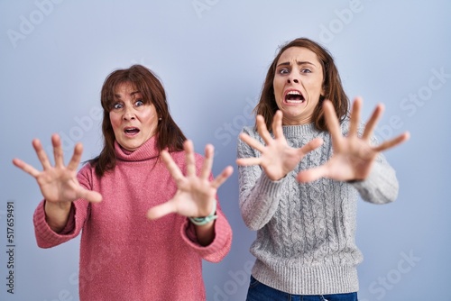 Fotografía Mother and daughter standing over blue background afraid and terrified with fear expression stop gesture with hands, shouting in shock