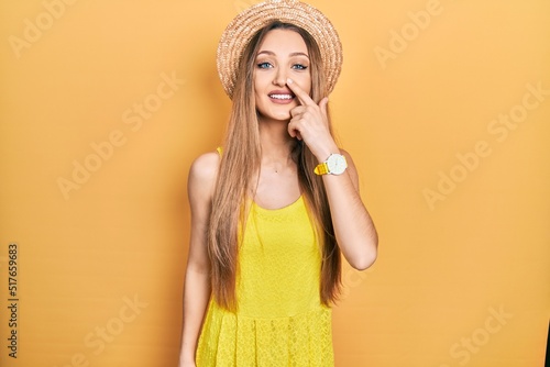 Young blonde girl wearing summer hat pointing with hand finger to face and nose, smiling cheerful. beauty concept