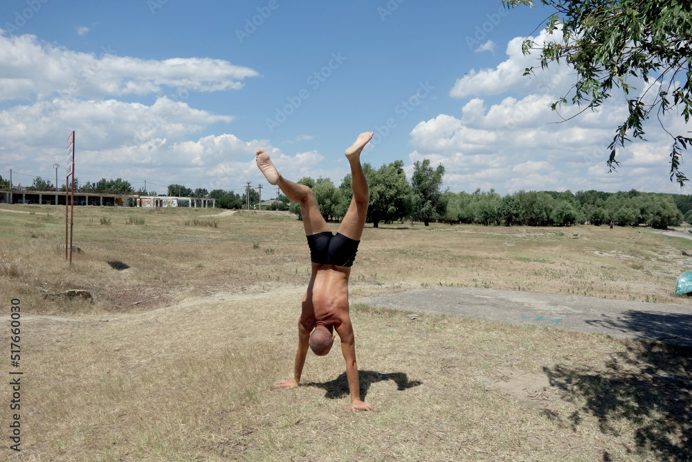 athletic man walking on his hands in nature in summer athletic man walking on his hands in nature in summer