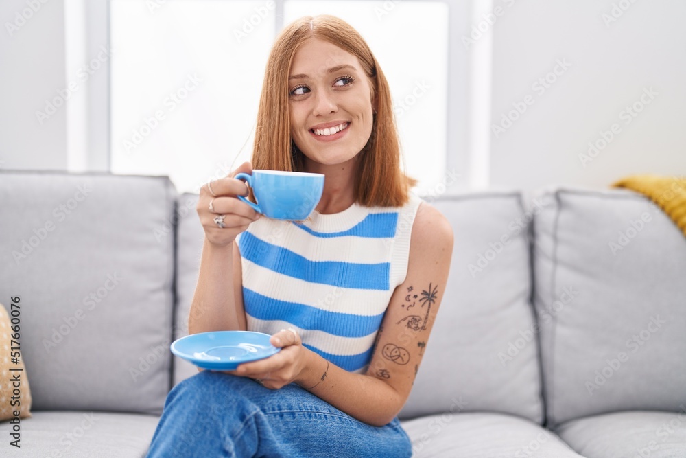 Young redhead woman drinking coffee sitting on sofa at home Young redhead woman drinking coffee sitting on sofa at home