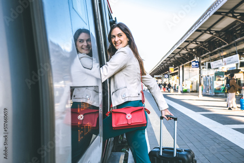 Young business woman standing on train door peeking out looking for somebody in railway station - Potrait of beautiful traveler woman getting on the train - Travelling concept