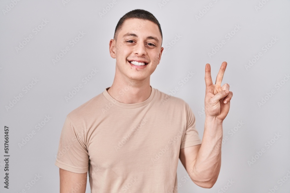 Young man standing over isolated background showing and pointing up with fingers number two while smiling confident and happy. Young man standing over isolated background showing and pointing up with fingers number two while smiling confident and happy.