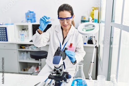 Young hispanic woman wearing scientist uniform using microscope at laboratory