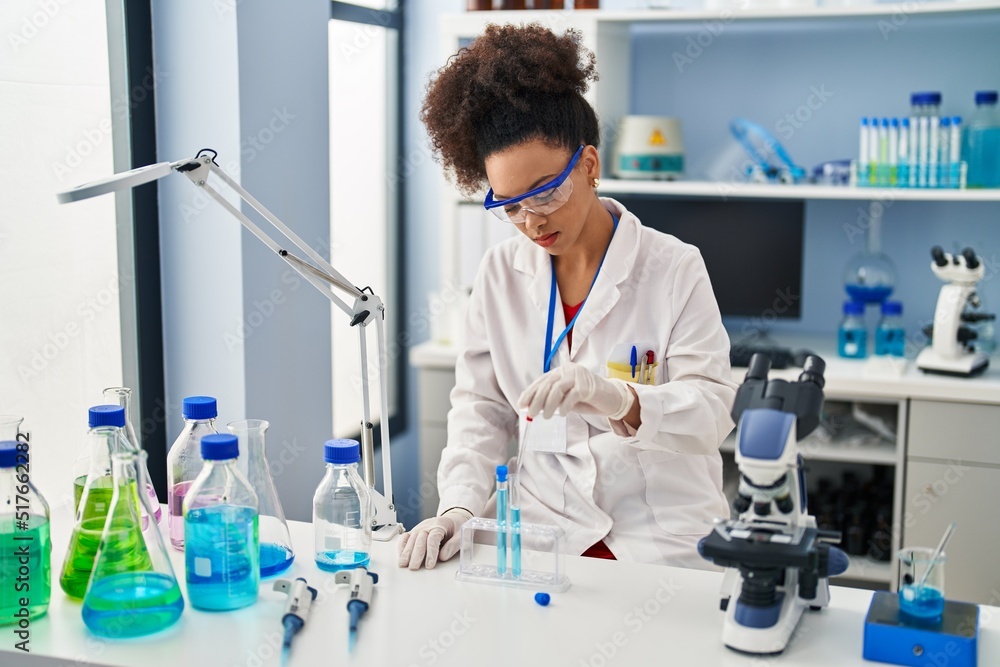 Young african american woman wearing scientist uniform using pipette working at laboratory Young african american woman wearing scientist uniform using pipette working at laboratory