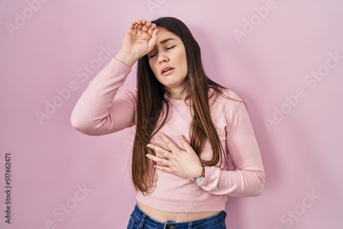 Young brunette woman standing over pink background touching forehead for illness and fever, flu and cold, virus sick