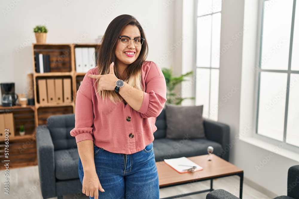 Young hispanic woman working at the office wearing glasses smiling cheerful pointing with hand and finger up to the side Young hispanic woman working at the office wearing glasses smiling cheerful pointing with hand and finger up to the side