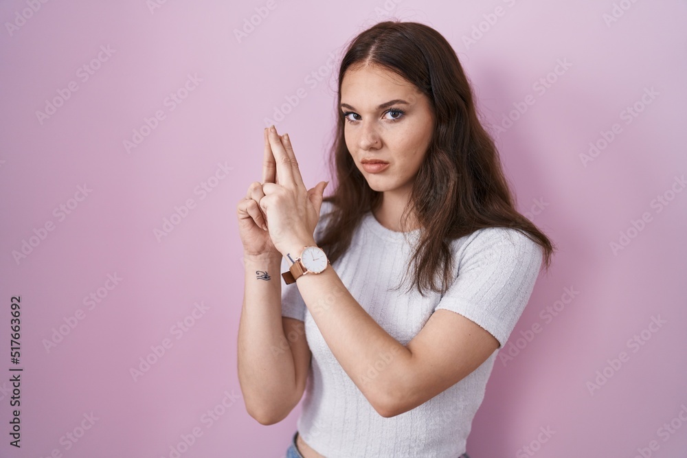 Young hispanic girl standing over pink background holding symbolic gun with hand gesture, playing killing shooting weapons, angry face Young hispanic girl standing over pink background holding symbolic gun with hand gesture, playing killing shooting weapons, angry face