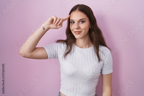 Young hispanic girl standing over pink background smiling pointing to head with one finger, great idea or thought, good memory