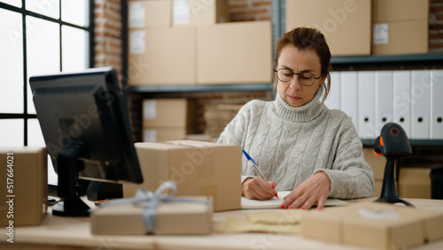 Middle age hispanic woman ecommerce business worker writing on book at storehouse office