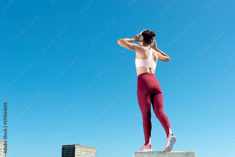 Rear view of a sporty woman holding heaphones on her head. rear view, urban background. Rear view of a sporty woman holding heaphones on her head. rear view, urban background.