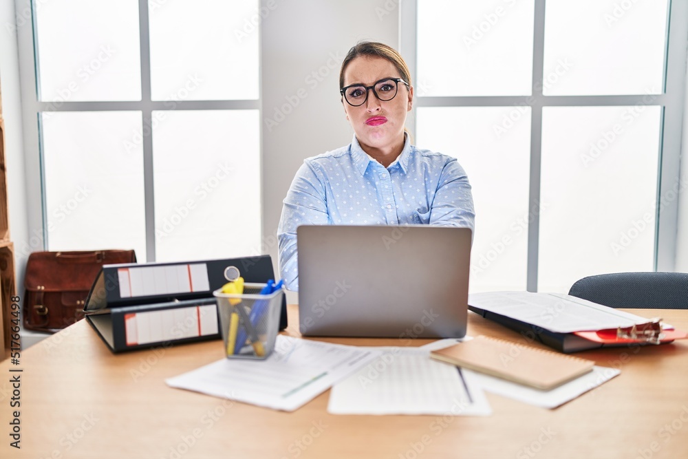 Fototapeta premium Young hispanic woman working at the office wearing glasses skeptic and nervous, disapproving expression on face with crossed arms. negative person.